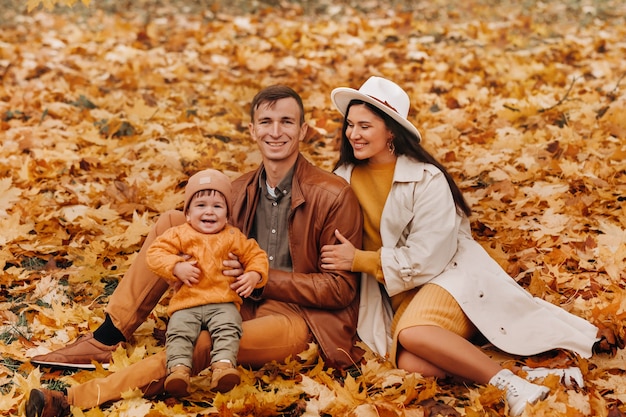 Father and mother with son sitting in the autumn Park. Portrait of a Golden autumn Family in a nature Park.