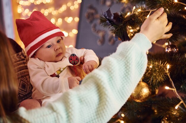 Photo father and mother with their child decorating tree together in room.