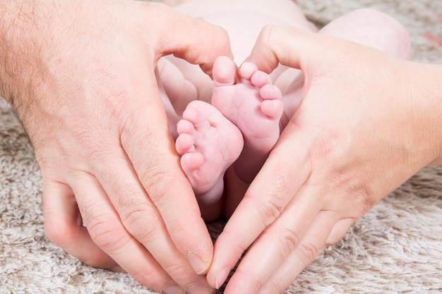 Father and mother with their hands form a heart around the feet of the new born baby