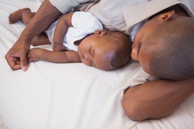 Father napping with baby son on couch