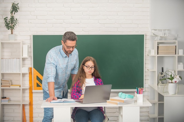 Father and nerd child study at school with laptop on blackboard background, estudy