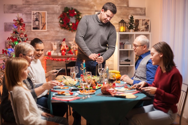father opening a bottle of wine at christmas family dinner. delicious food.