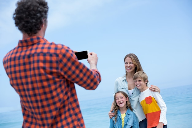 Father photographing cheerful family at beach