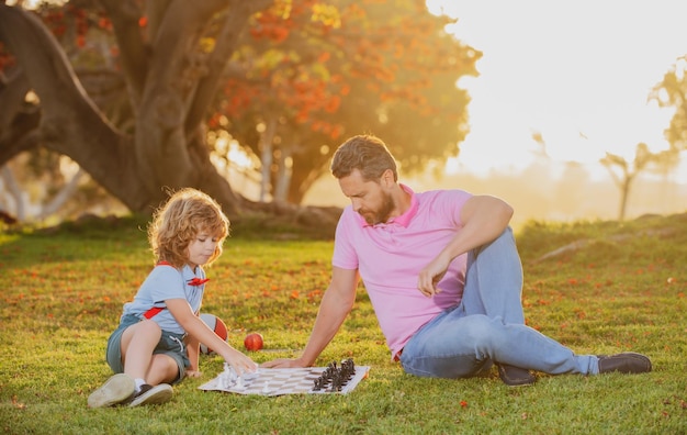 Father play chess with son thinking child while playing chess family outside game