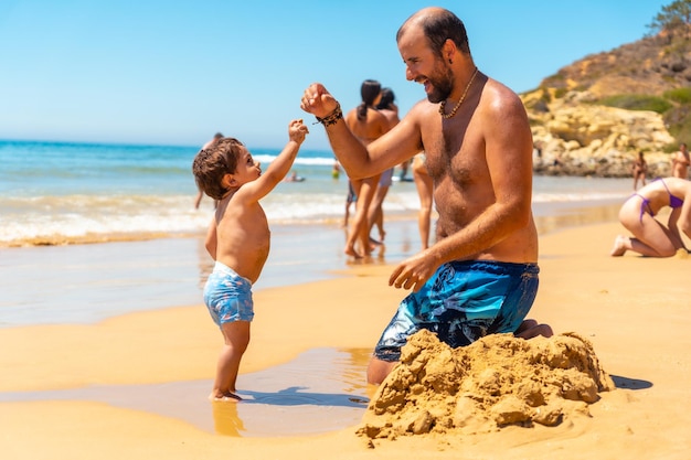 아버지는 모래에서 놀고 아들 Praia do Barranco das Belharucas 해변 Albufeira Algarve Portugal과 즐거운 시간을 보내고 있습니다.