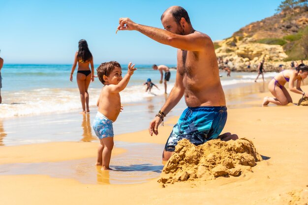 아들 Praia do Barranco das Belharucas 해변 Albufeira Algarve Portugal과 모래에서 노는 아버지