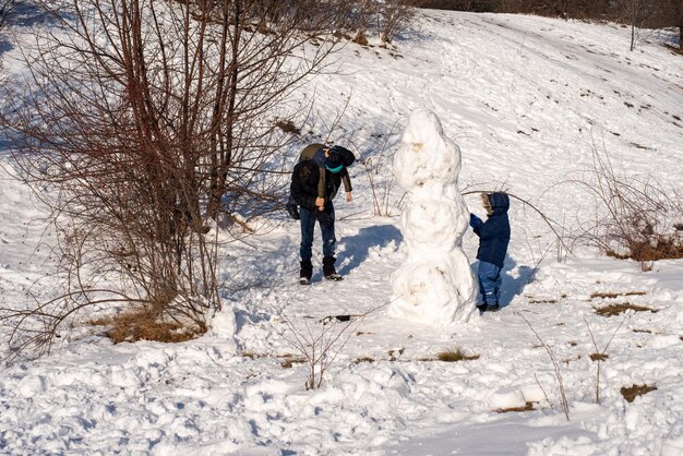 写真 公園で雪だるまの遊びをしている父親と子供たち ⁇