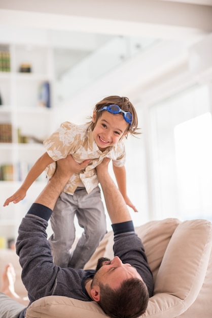 彼の小さな息子と家庭のソファで遊んでいる父