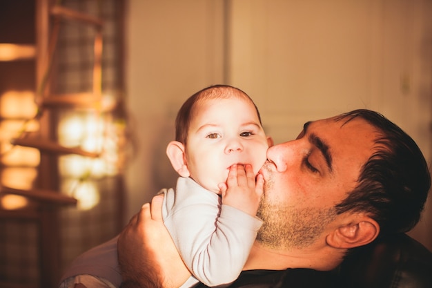 Father playing with son and kissing baby holding him in her arms