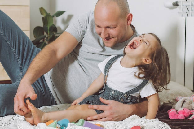 Father plays with little daughter 2-4 on floor. Dad tickles kids feet. Family, having fun