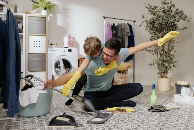 Father plays with son in laundry room while cleaning man is holding kid on back