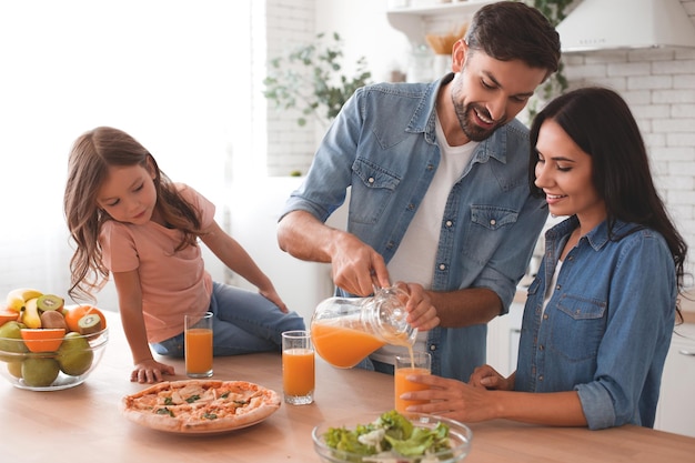 Father pouring orange juice into the glasses for daughter and wife in the kitchen