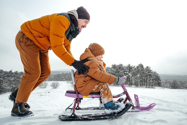 Father pulling little son on sledge in winter