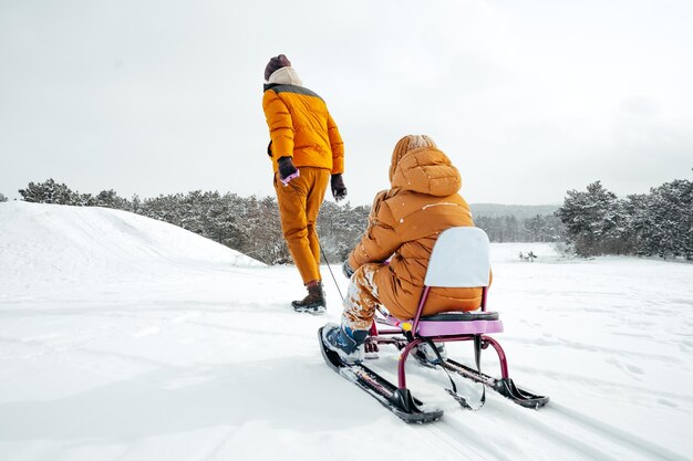 Father pulling little son on sledge in winter