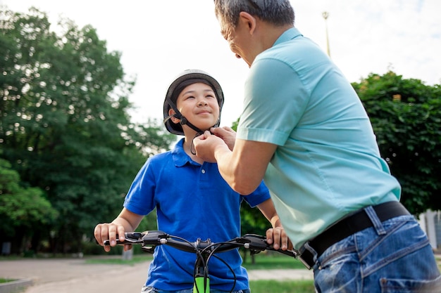 Father puts protective helmet on his Asian son's head Korean boy rides bike with dad