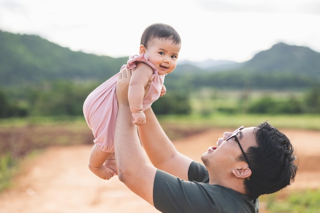 Father raises his daughter is not yet a year old lift up in the sky. Father holding daughter in arms. Happy asian family child and dad walking outdoor nature. Happy Father's Day