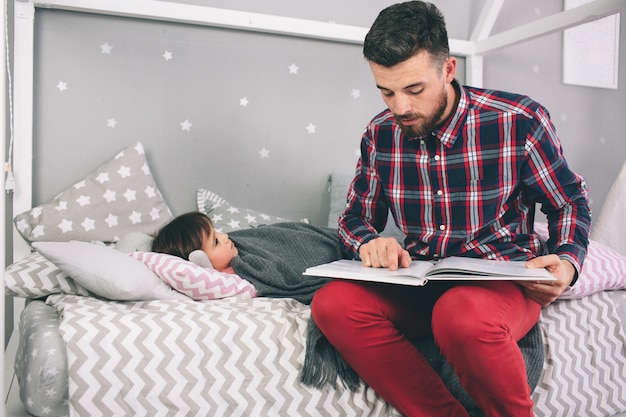 Отец читает книгу своей дочери, лежа на кровати в спальне