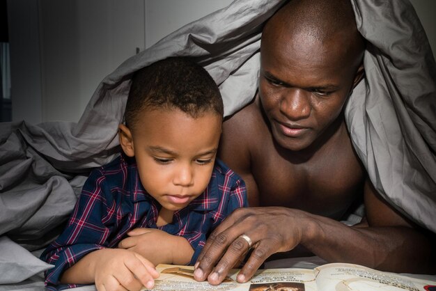 Foto padre che legge un libro per suo figlio sotto la coperta