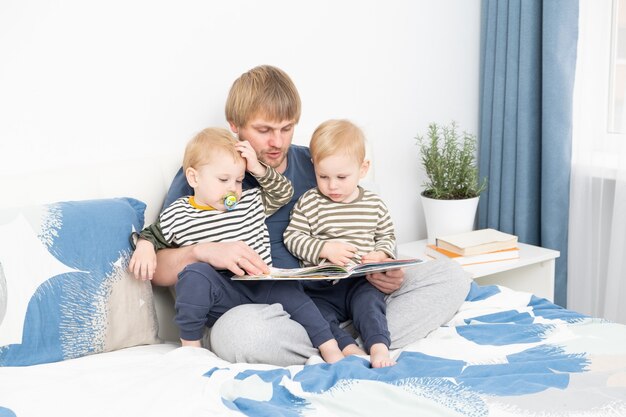 Father reading a book to his sons twins on bed at home spending time together