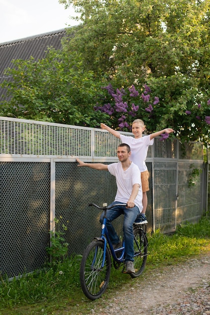 A father rides his son in a white Tshirt on a bicycle The happy son spread his arms