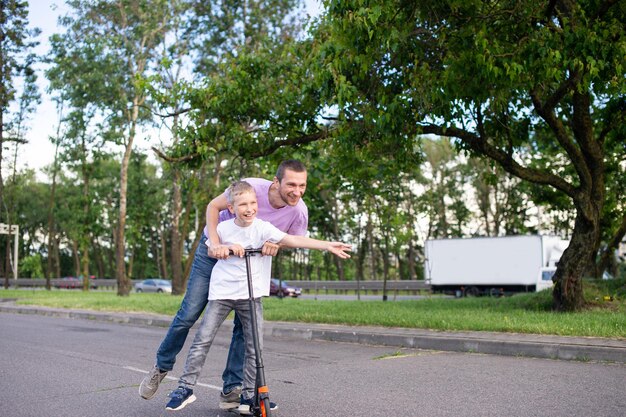 A father rides his son in a white Tshirt on a scooter the happy child spread his hands