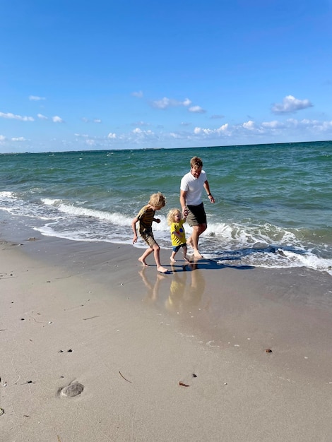 Foto un padre che corre sulla spiaggia con i suoi figli