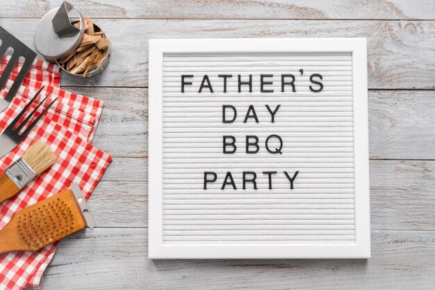 Father's Day BBQ Party sign on a white memo board with cooking tools.