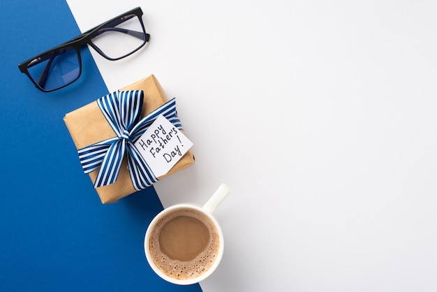 아버지의 날 개념 리본 활과 엽서 안경, 빈 공간이 있는 바이콜러 파란색과 흰색 배경에 커피 한 잔이 있는 공예 종이 선물 상자의 상위 뷰 사진