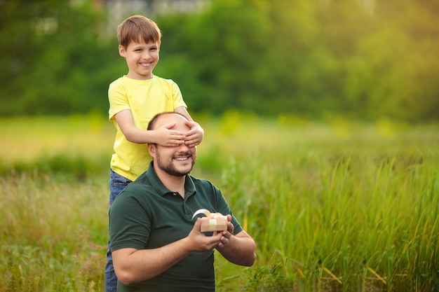 父の日。幸せな父と息子は自然の中で一緒に時間を過ごす、子供は父親に贈り物を与える