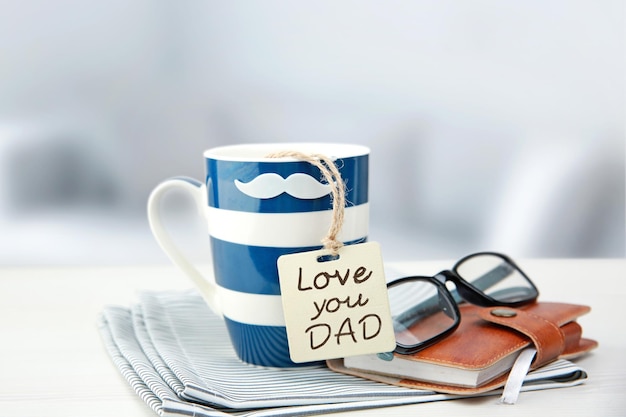 Photo father's day holiday greeting cardmug tea coffee and present gift box tag on wooden table blur light