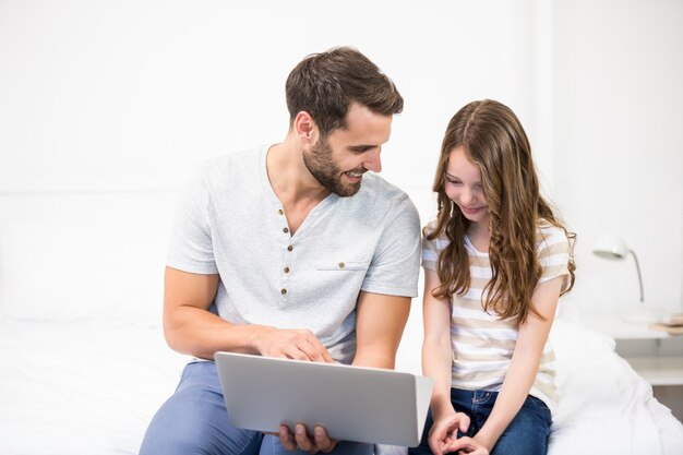 Father showing laptop to daughter on bed