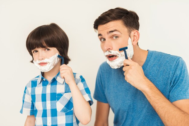 The father shows his son how to shave in the bathroom.