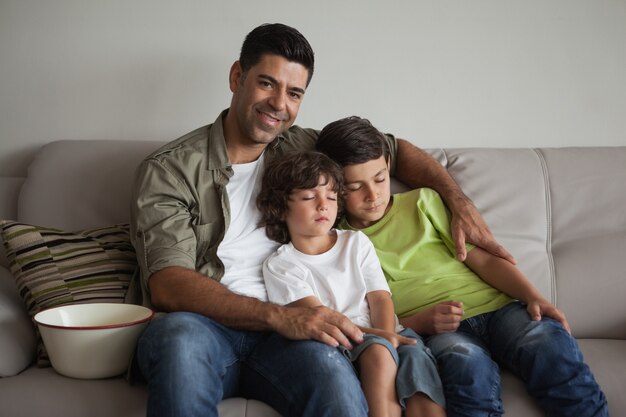 Father and sleepy sons with popcorn bowl watching tv in living room