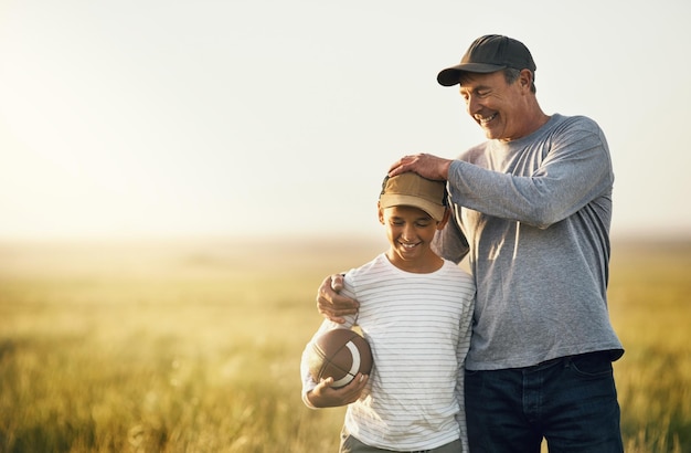 写真 自然の中で絆を深め、楽しむための田舎の野原にある父と息子とラグビーボール。幸せと笑顔を持った父と幼い子供をモックアップし、農場で屋外でアメリカンフットボールの試合を始める準備ができている