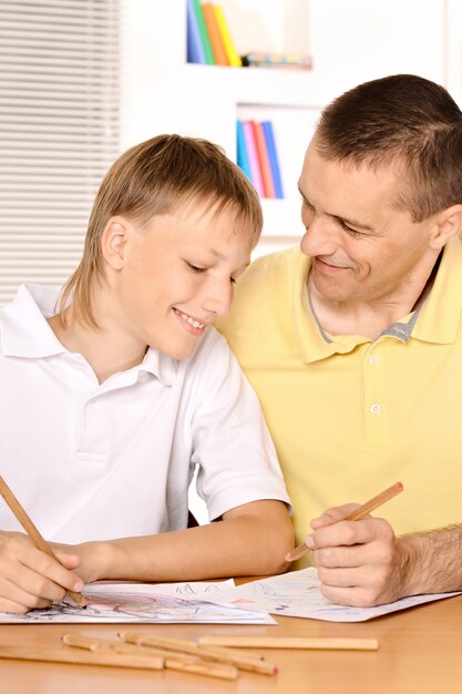 Father and son are drawing together with pencil at table