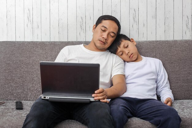 Father and son are fall asleep in sitting position on the sofa when learning online using laptop