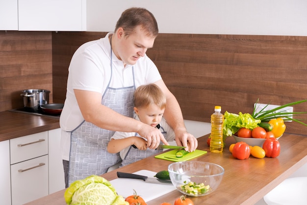 Father son are preparing fresh vegetables in kitchen dad and boy child cut
