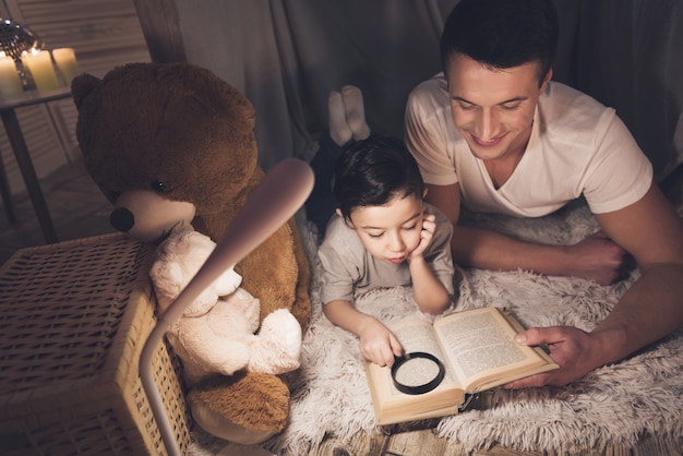 Father and son are reading book at night at home.