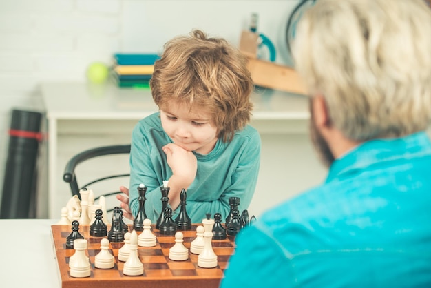 Father and son boy with father teaching and learning chess at home home tutor helping boy with studi...