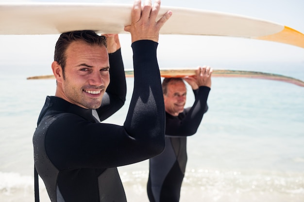 Padre e figlio che trasportano una tavola da surf sopra la testa