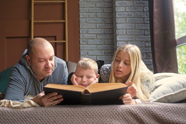 Photo father, son and daughter read a book in bed