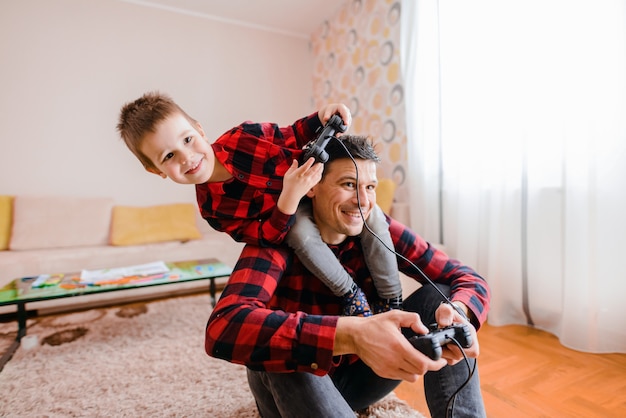 Father and son day . Cheerful father and son playing video games. Son is sitting on father shoulders.