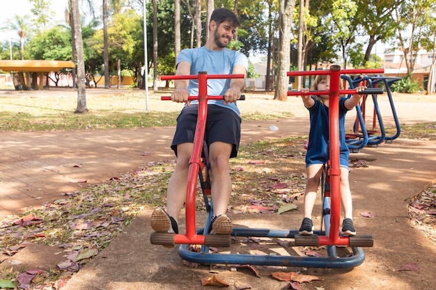 Father and son doing exercise on apparatus outdoors with daughter