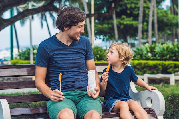 Father and son eat fried sweet potatoes in the park.