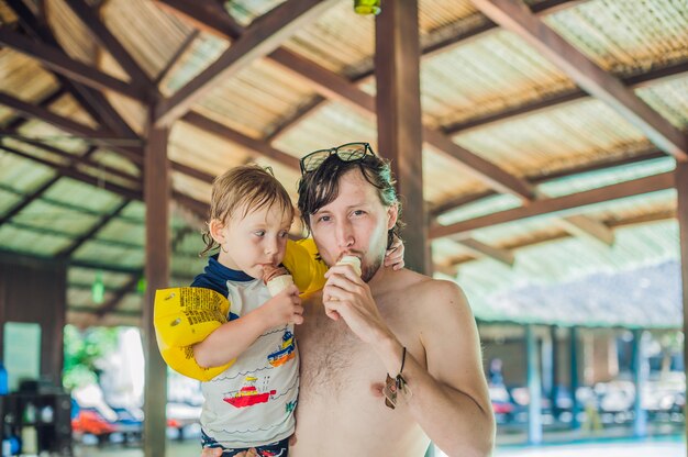 Padre e figlio che mangiano il gelato nel aquapark sotto un tetto ricoperto di paglia