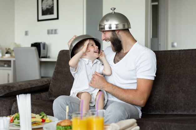 Father and son have breakfast in a hotel room and indulge, laugh.