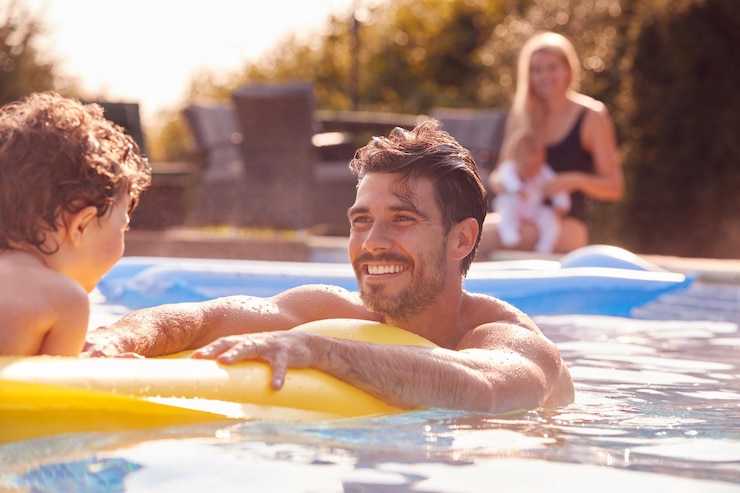 Photo father and son have fun playing in outdoor pool on vacation as mother and baby watch from side