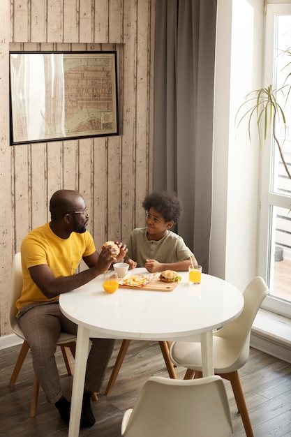 Photo father and son having french fries and burgers together