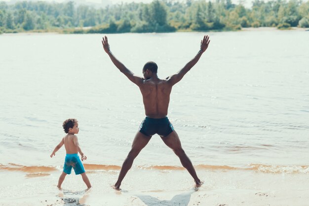 Father and Son is Exercising in Water on River Shore