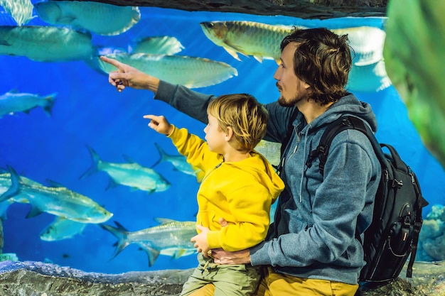 Отец и сын смотрят на рыбу в аквариуме океанариума